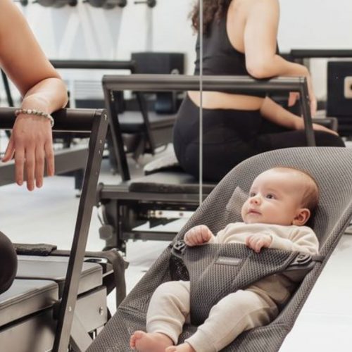 Baby in a BabyBjörn bouncer beside a Reformer during a postnatal Pilates class in Munich